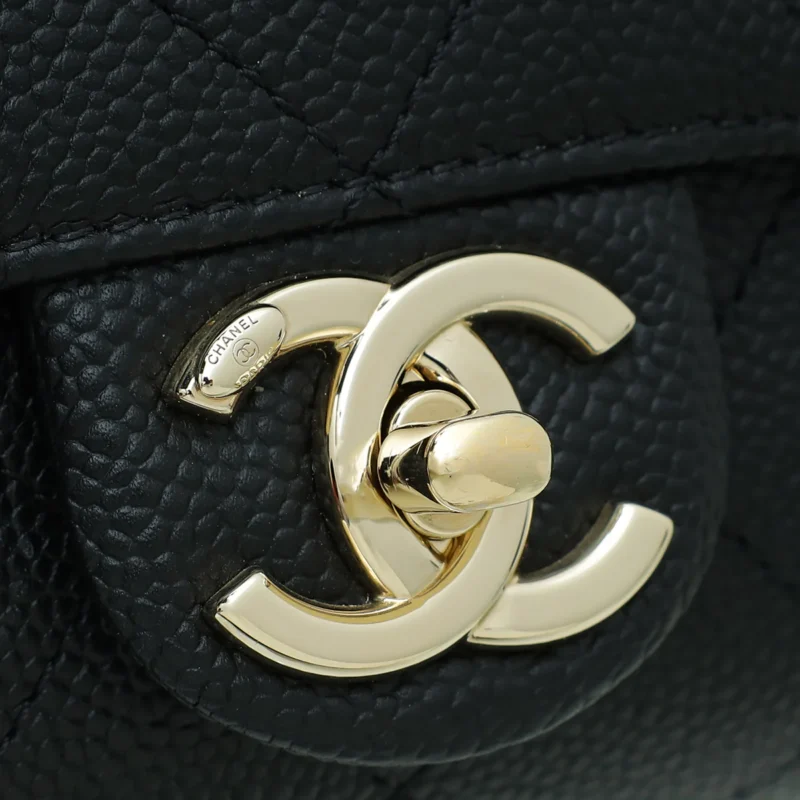 Close-up of a black leather handbag with a prominent gold double C logo2 clasp, featuring a quilted pattern on the leather.