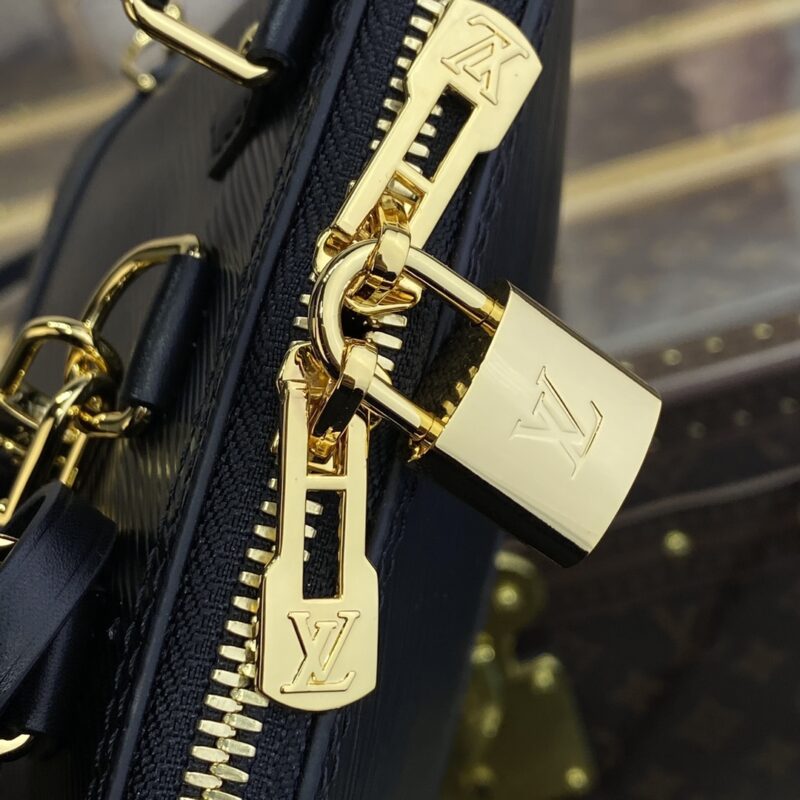 Close-up of a gold padlock attached to a zipper on a luxury black leather bag with gold details. The lock and zipper pulls feature engraved logo2s.